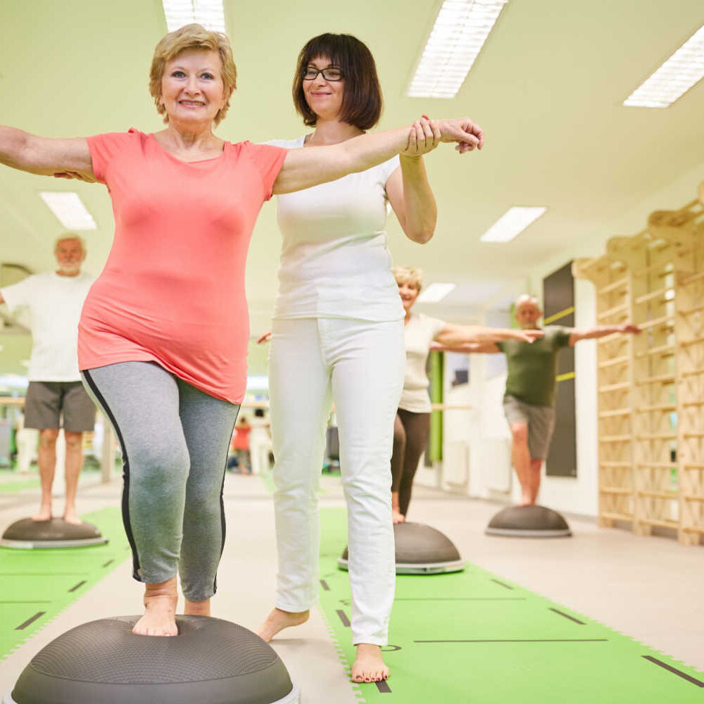 stock-photo-trainer-gives-senior-help-with-balance-training-at-the-bosu-ball-in-the-fitness-class-1557324209