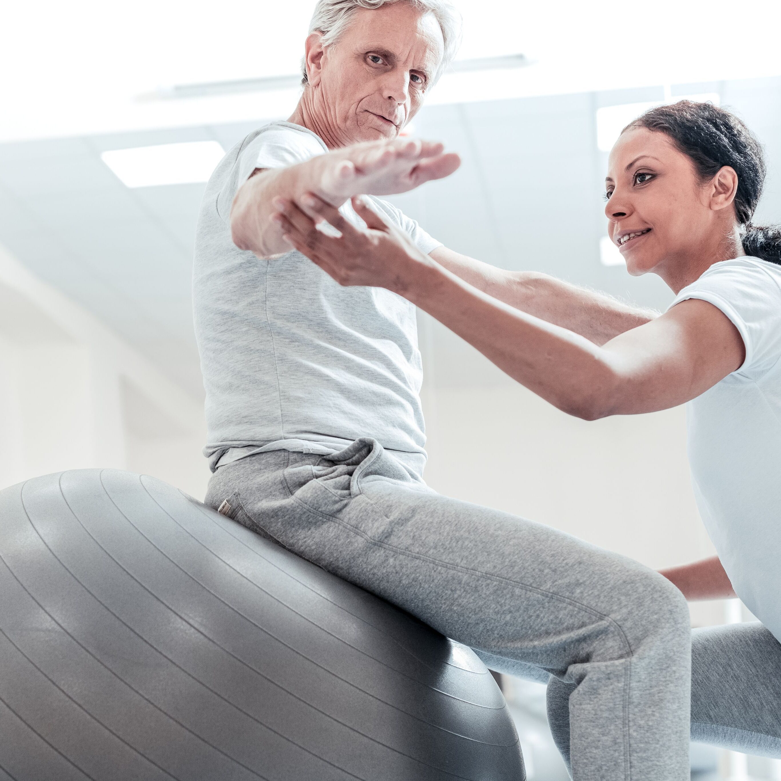 stock-photo-very-good-determined-old-wrinkled-grey-haired-man-sitting-on-a-ball-for-exercises-and-a-pretty-1028463184